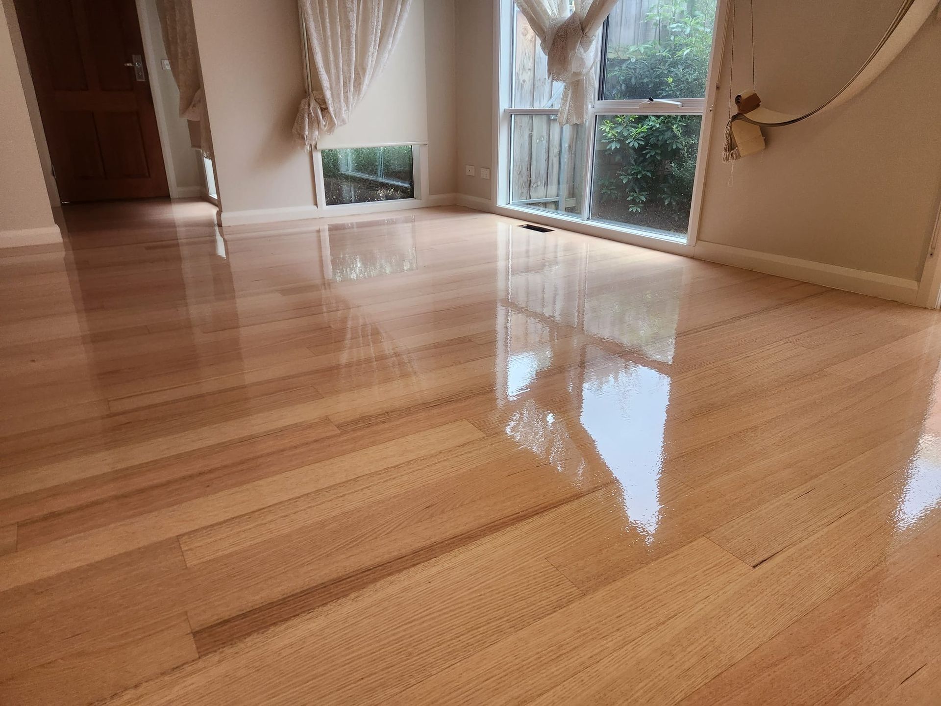Empty room with glossy wooden floors and large windows reflecting daylight