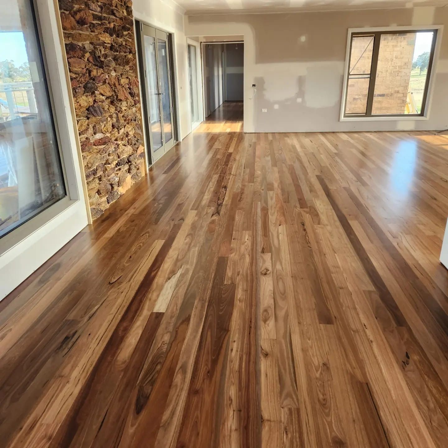 Empty modern room with polished wood floors, stone accent wall, and large windows overlooking trees