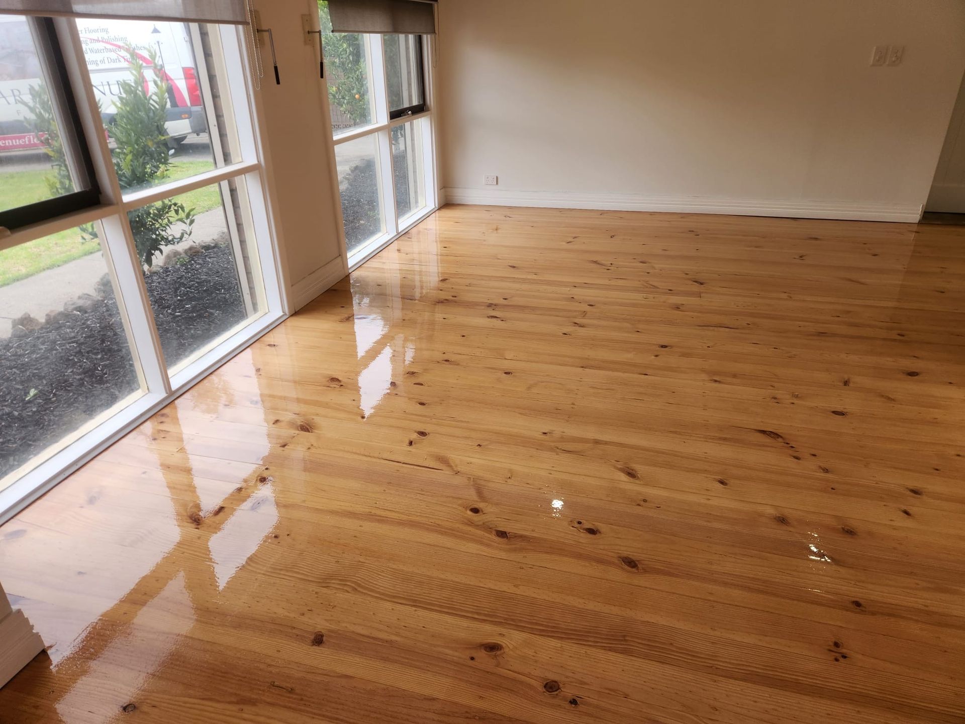 Empty room with polished wooden floor and large windows overlooking a wet outdoor area