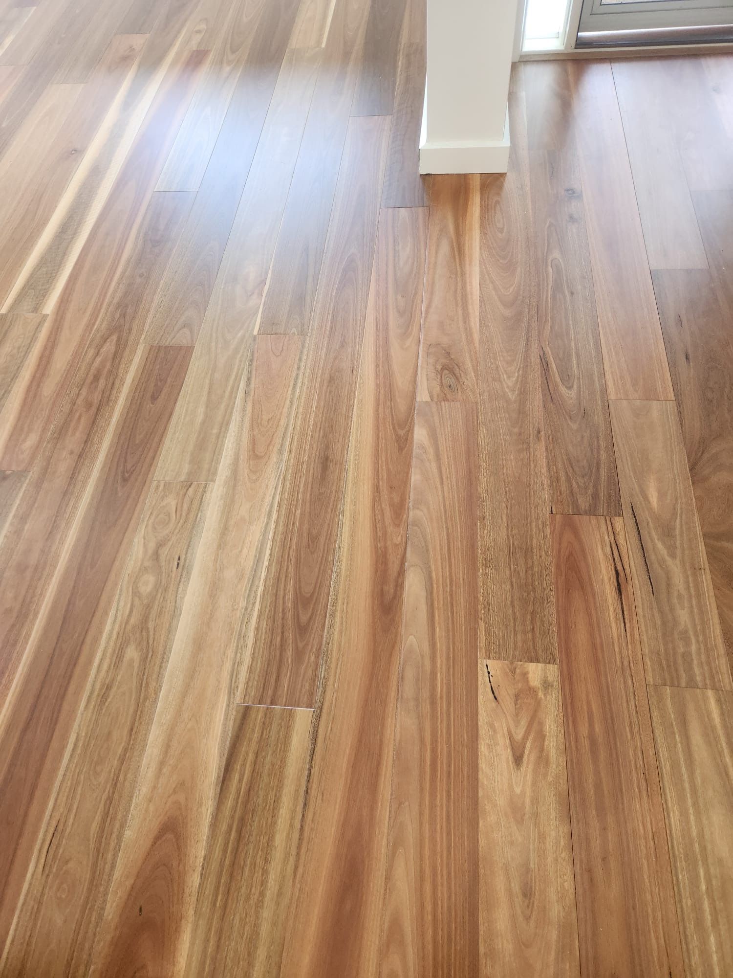 Light wood laminate floor with sunlight and a white wall column in the background