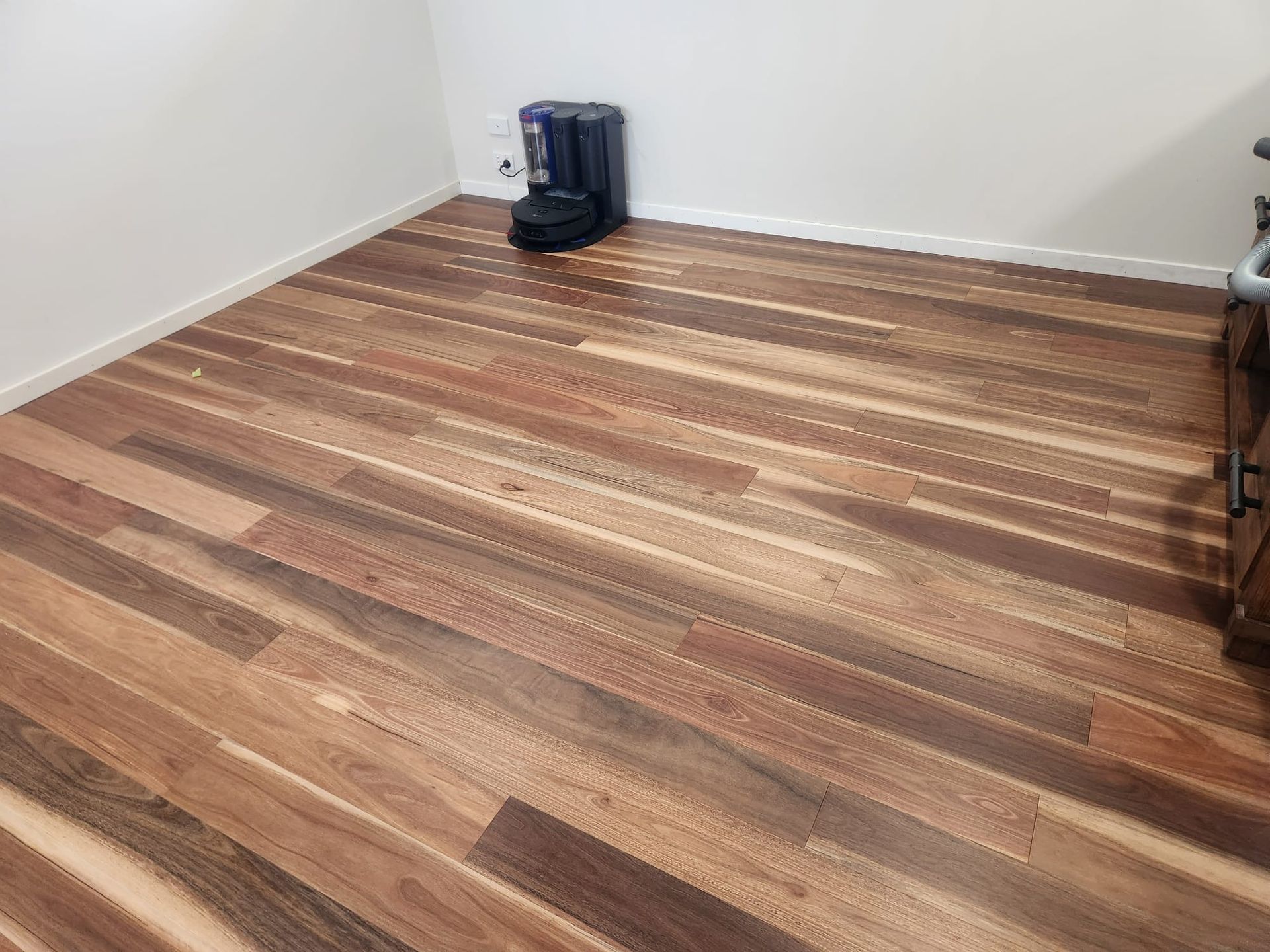 Empty room with wooden floor and a small black vacuum cleaner in the corner