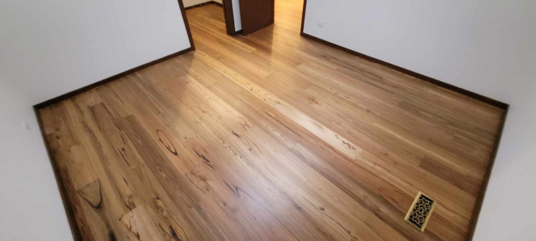 Empty room with wood floor, white walls, dark trim, and a floor vent.