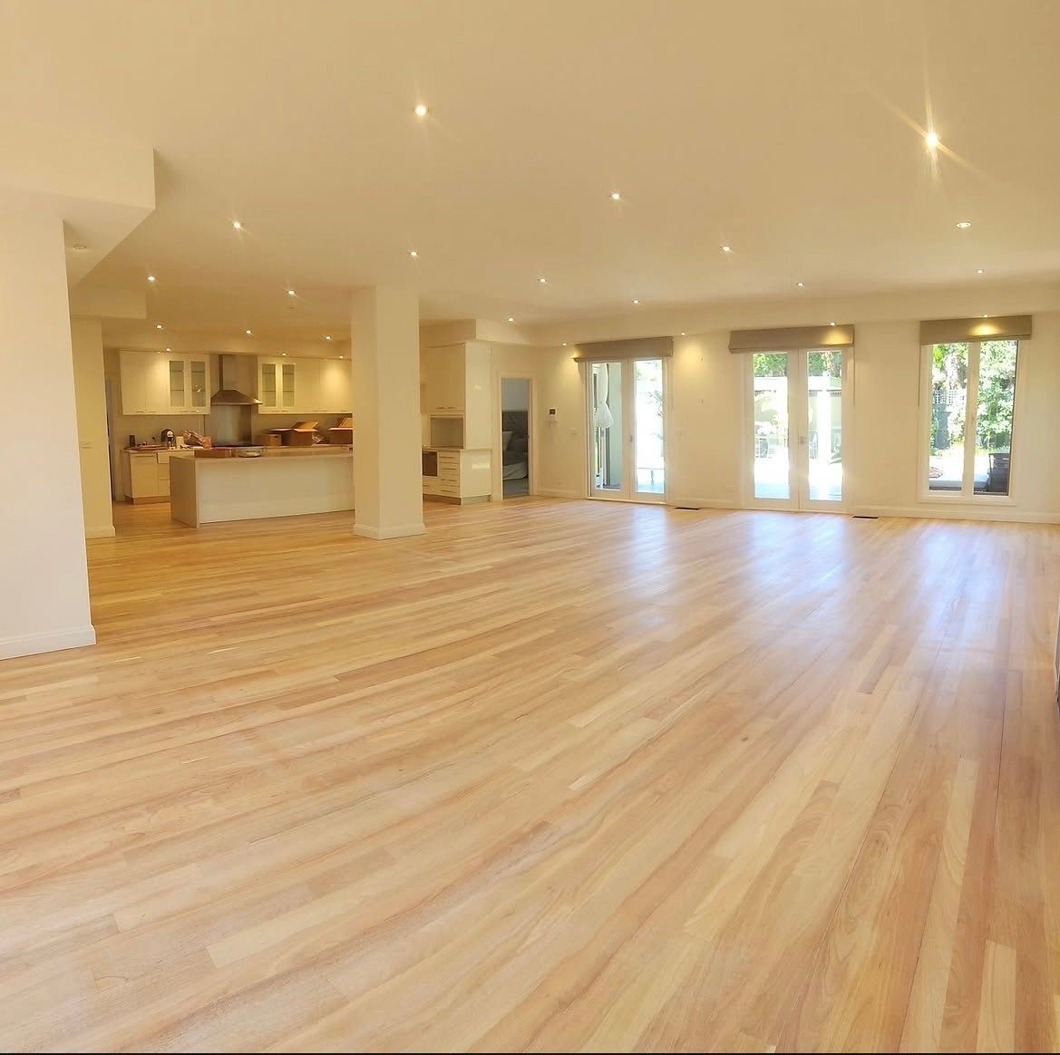 Spacious empty modern living room with light wood floors, recessed lighting, and large windows.