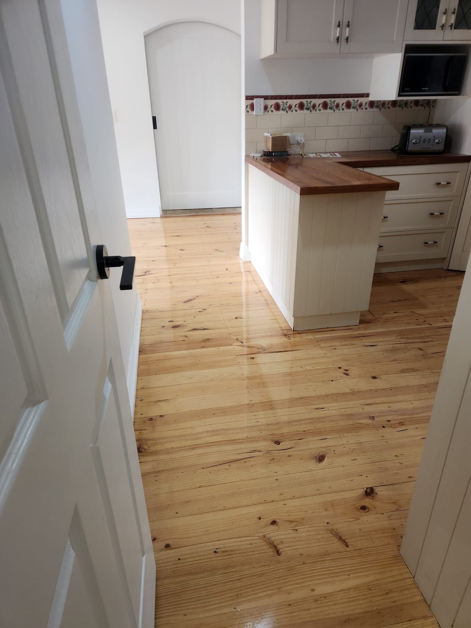 Bright kitchen with light wood floor, white cabinets, and a wooden countertop view from a doorway