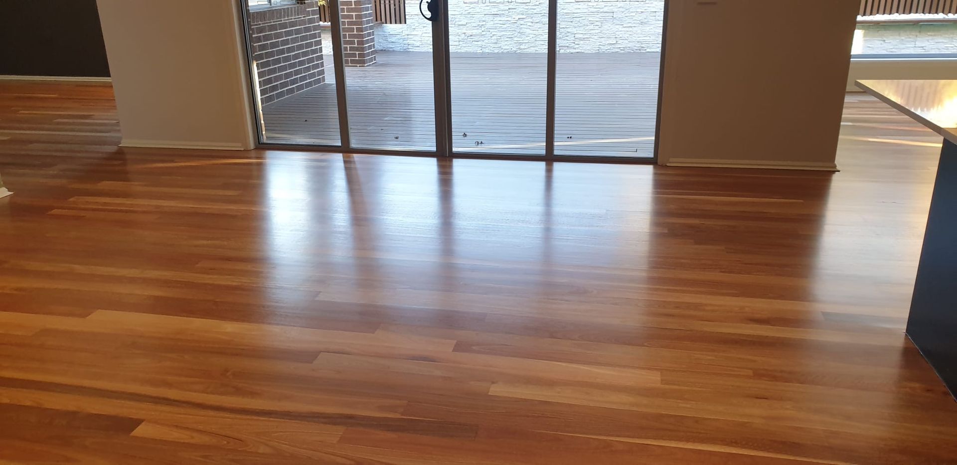 Empty polished hardwood floor by glass doors with light coming in from outside