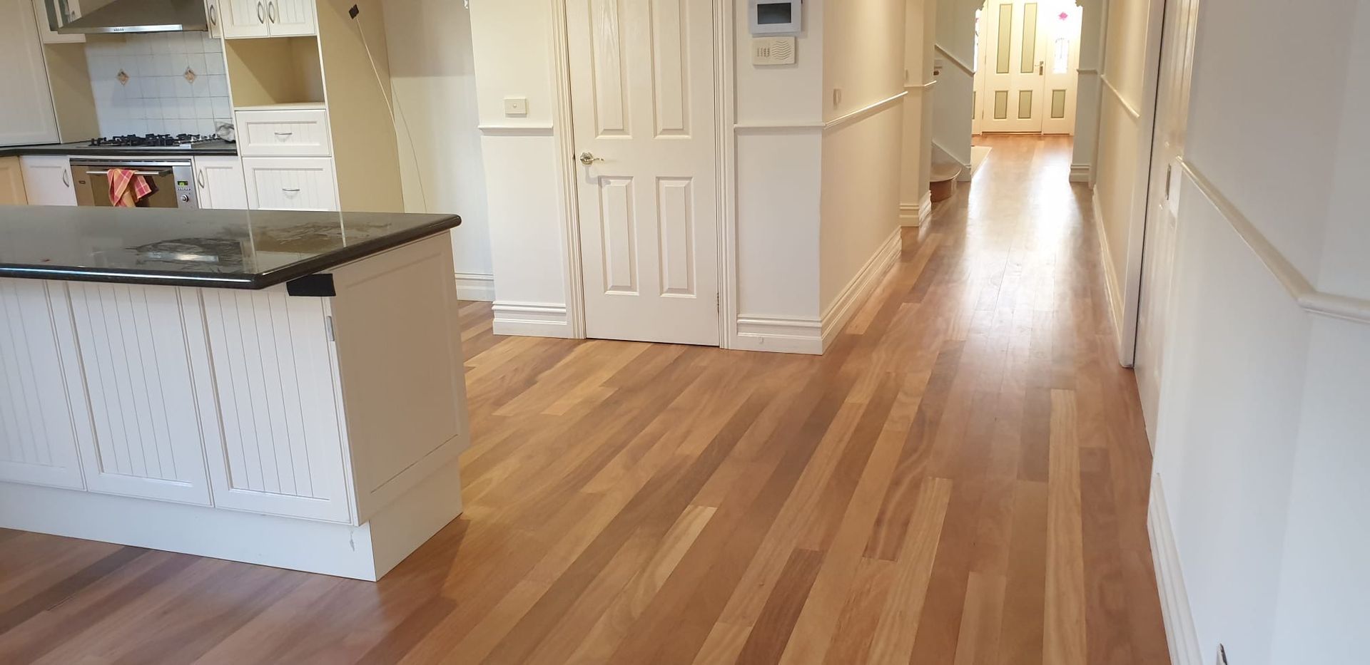 Bright hallway with hardwood floors, white walls, and a kitchen island on the left.