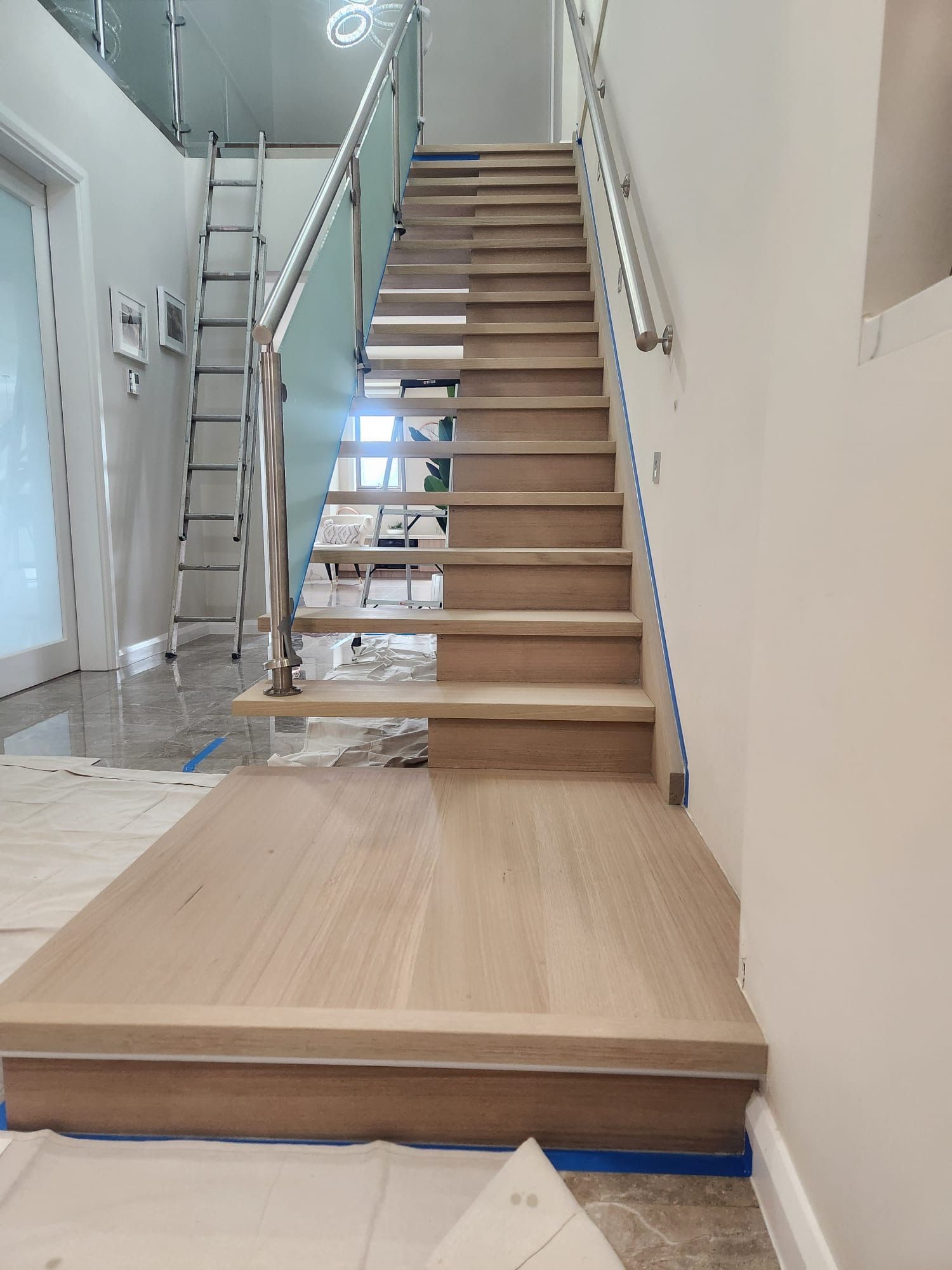 Indoor staircase under construction with wooden steps, metal railings, and a ladder on the left.