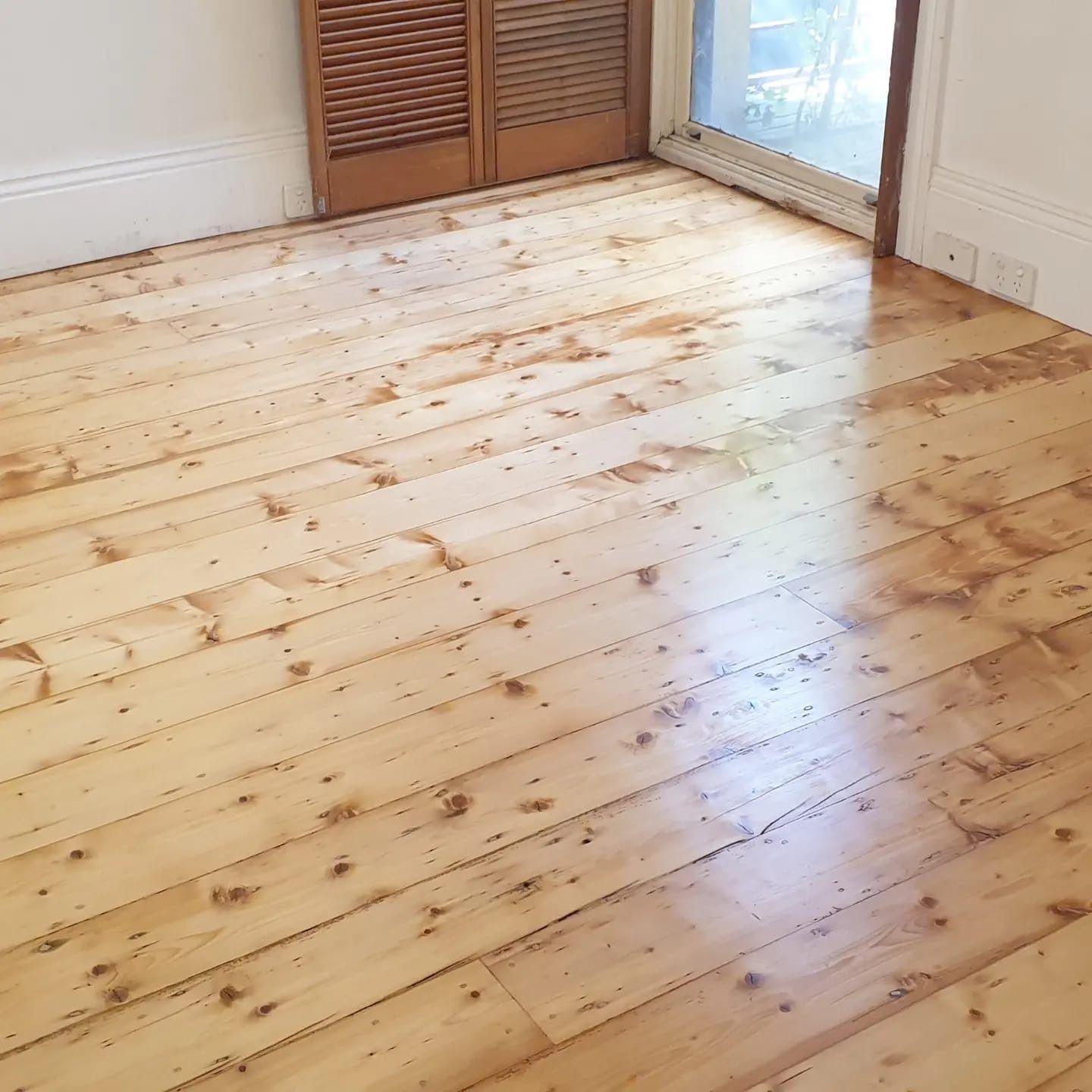 Empty room with light wood floor, white walls, closet doors, and a glass door letting in sunlight