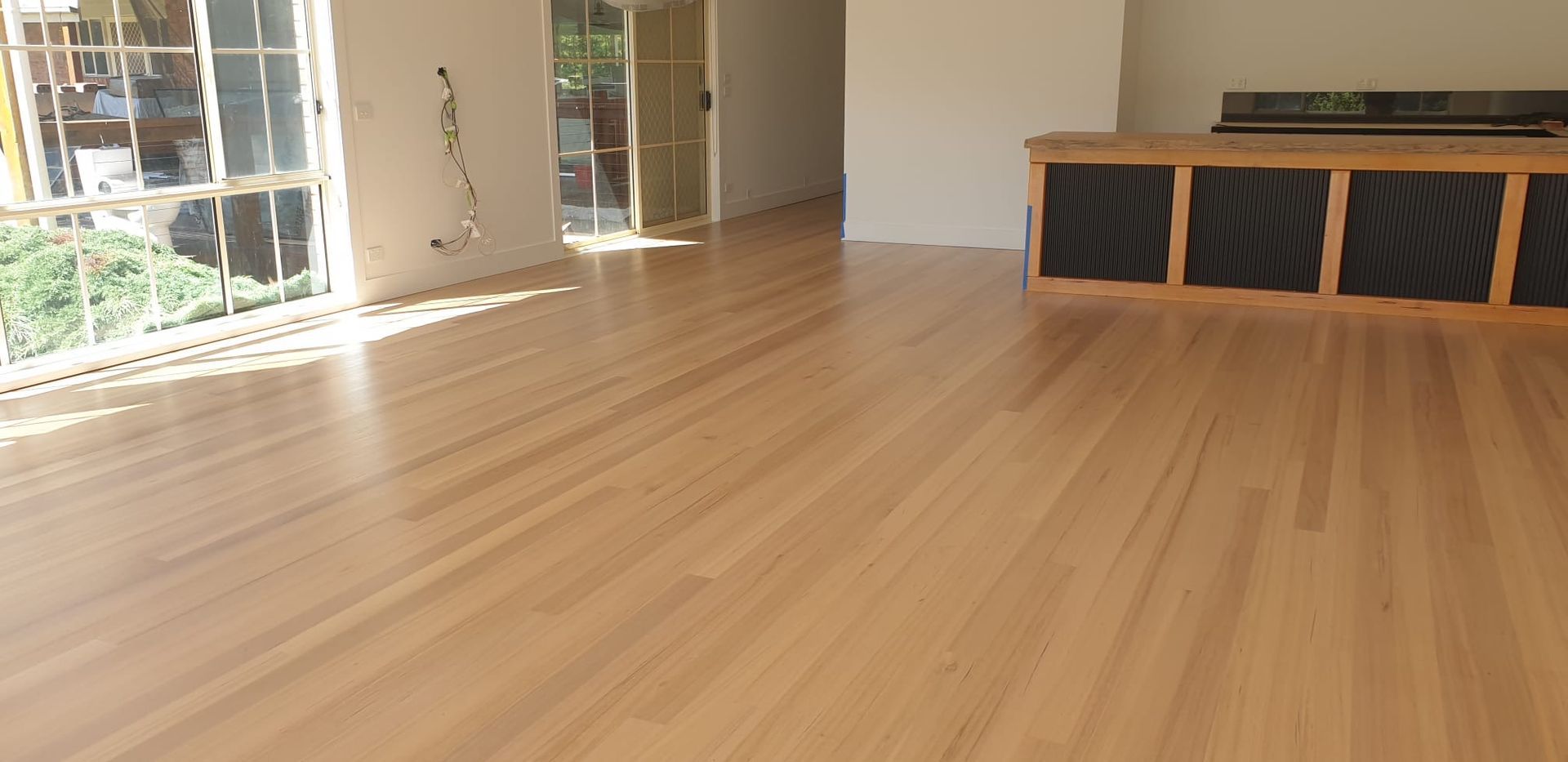 Empty living room with light wood floors, large windows, and a black storage bench along the wall