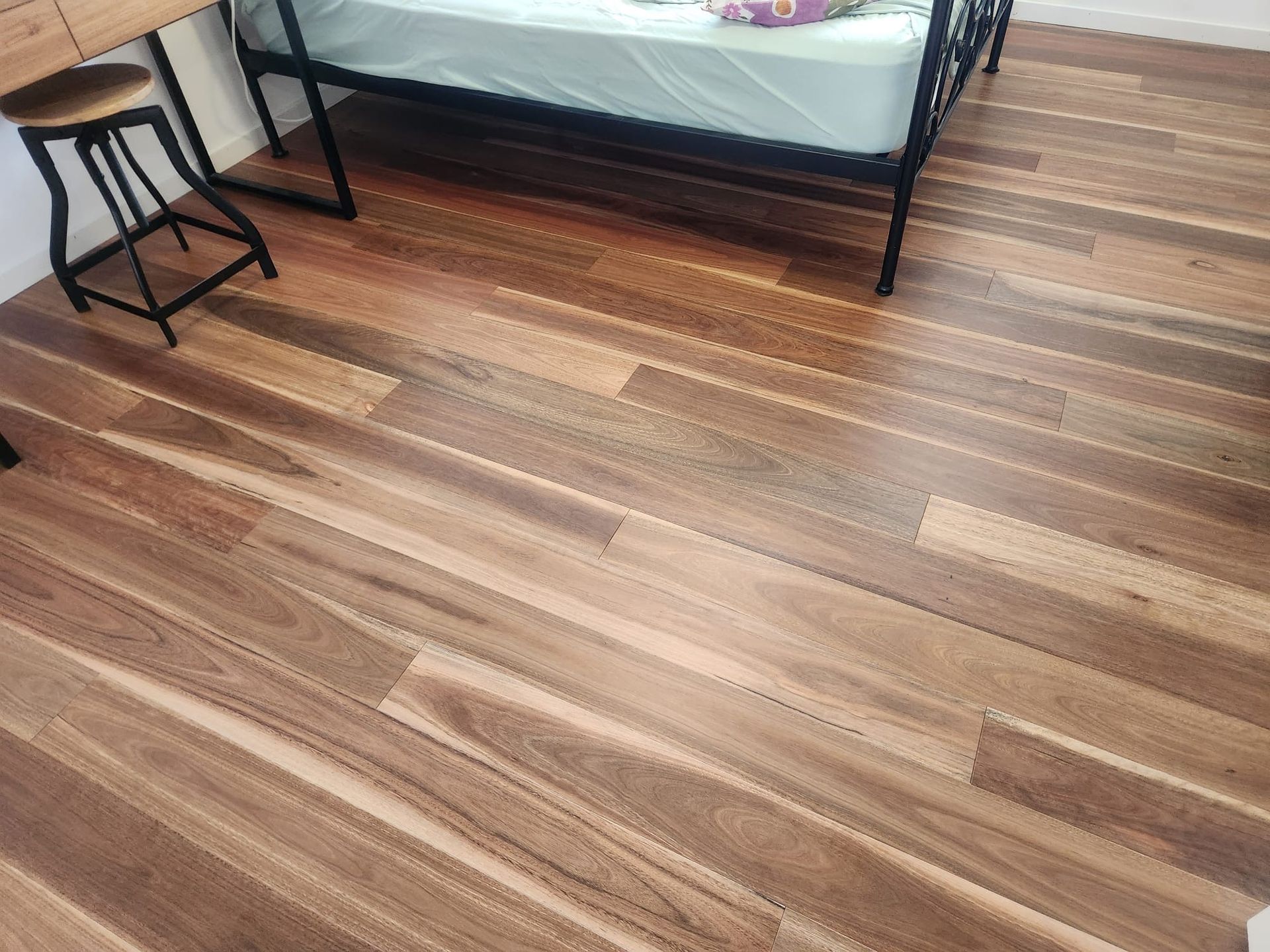 Wooden floor beside a bed and small black side table in a bedroom
