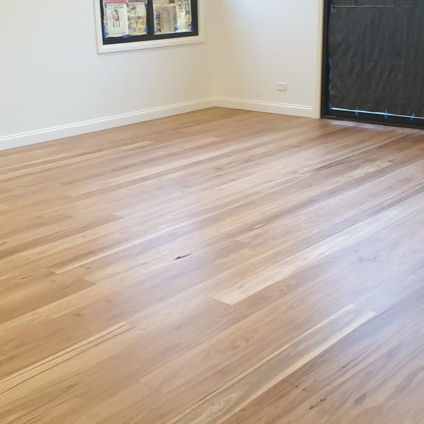 Empty room with light wood floor, white walls, wall art, and a large dark window blind.