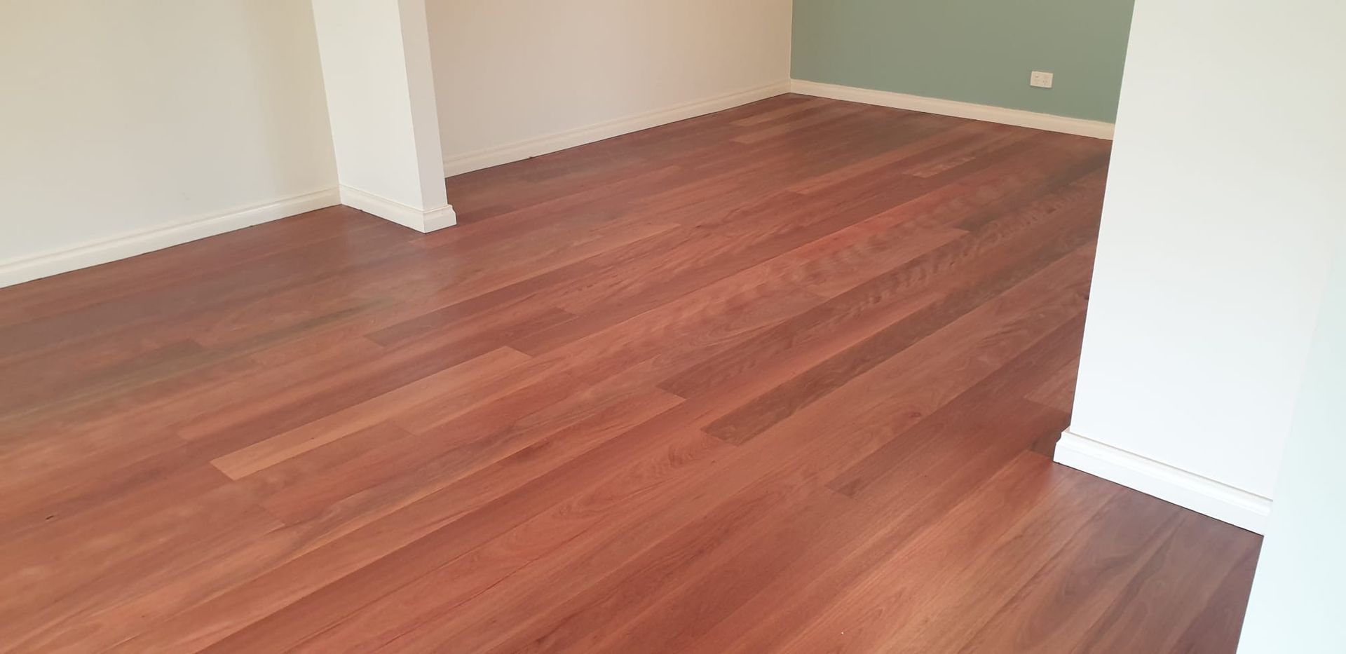 Empty room with hardwood floors, white walls, and a pale green accent wall.