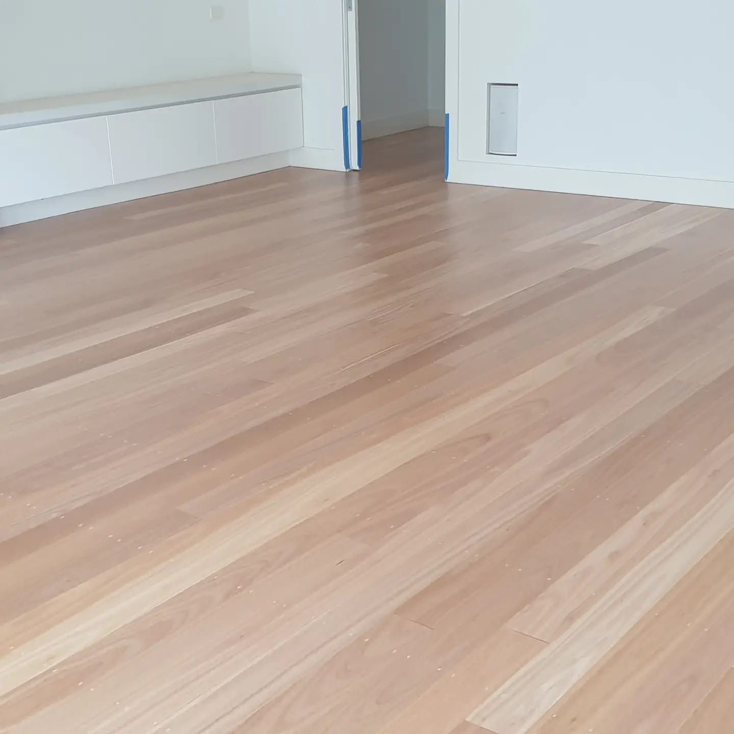 Empty room with light wood floors, white walls, and a small wall vent near the doorway.