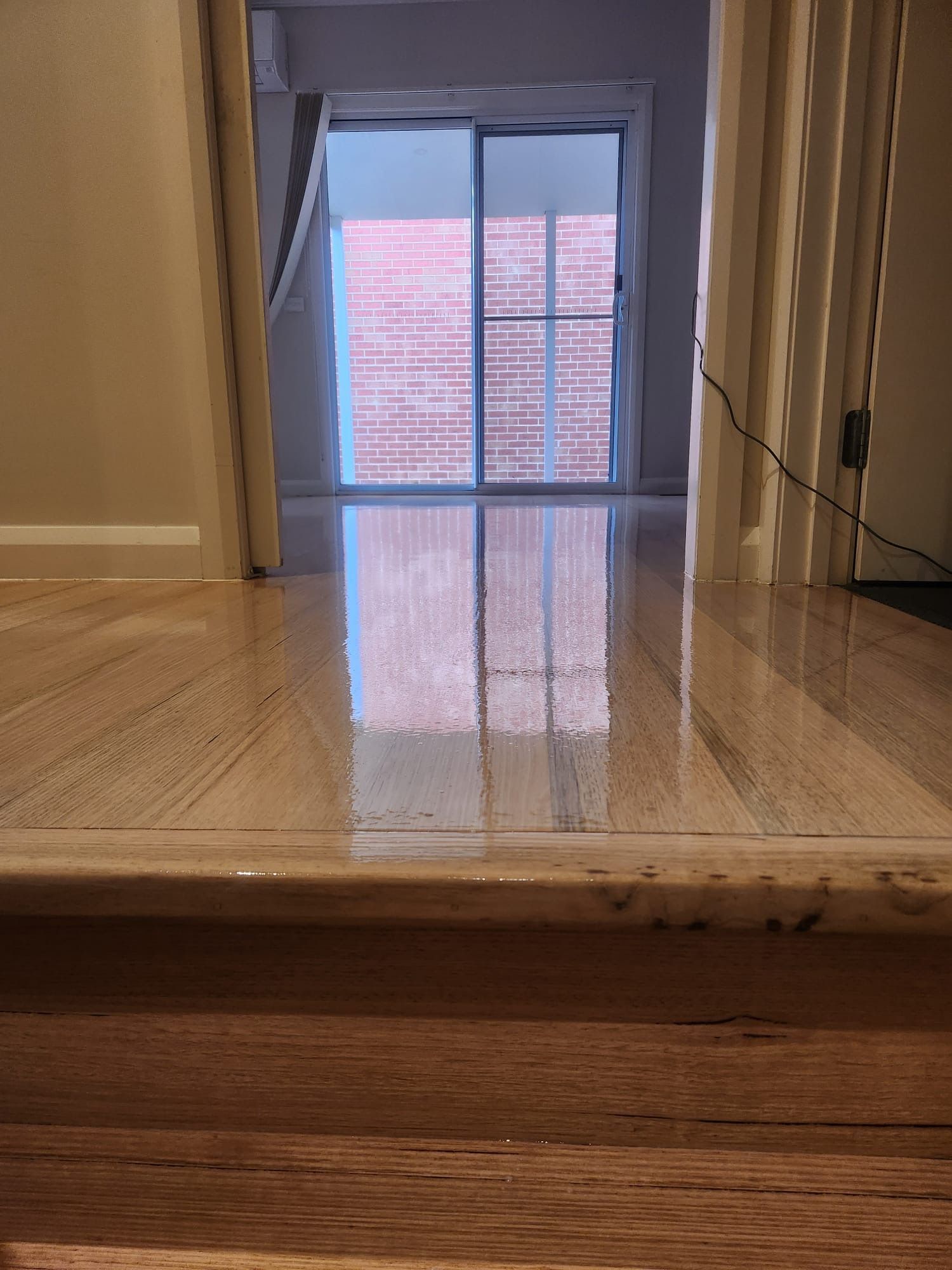 Shiny hardwood floor reflecting a sliding glass door and brick patio beyond, viewed from an upstairs landing