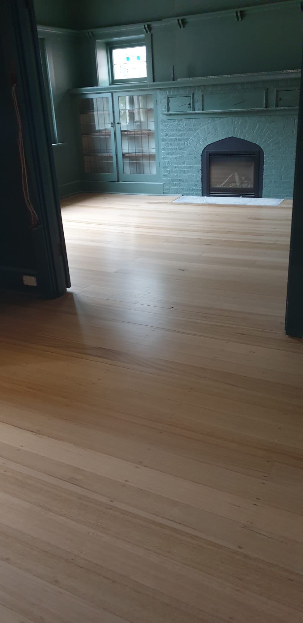 Empty room with a light wood floor, green walls, and a tiled fireplace on the far wall