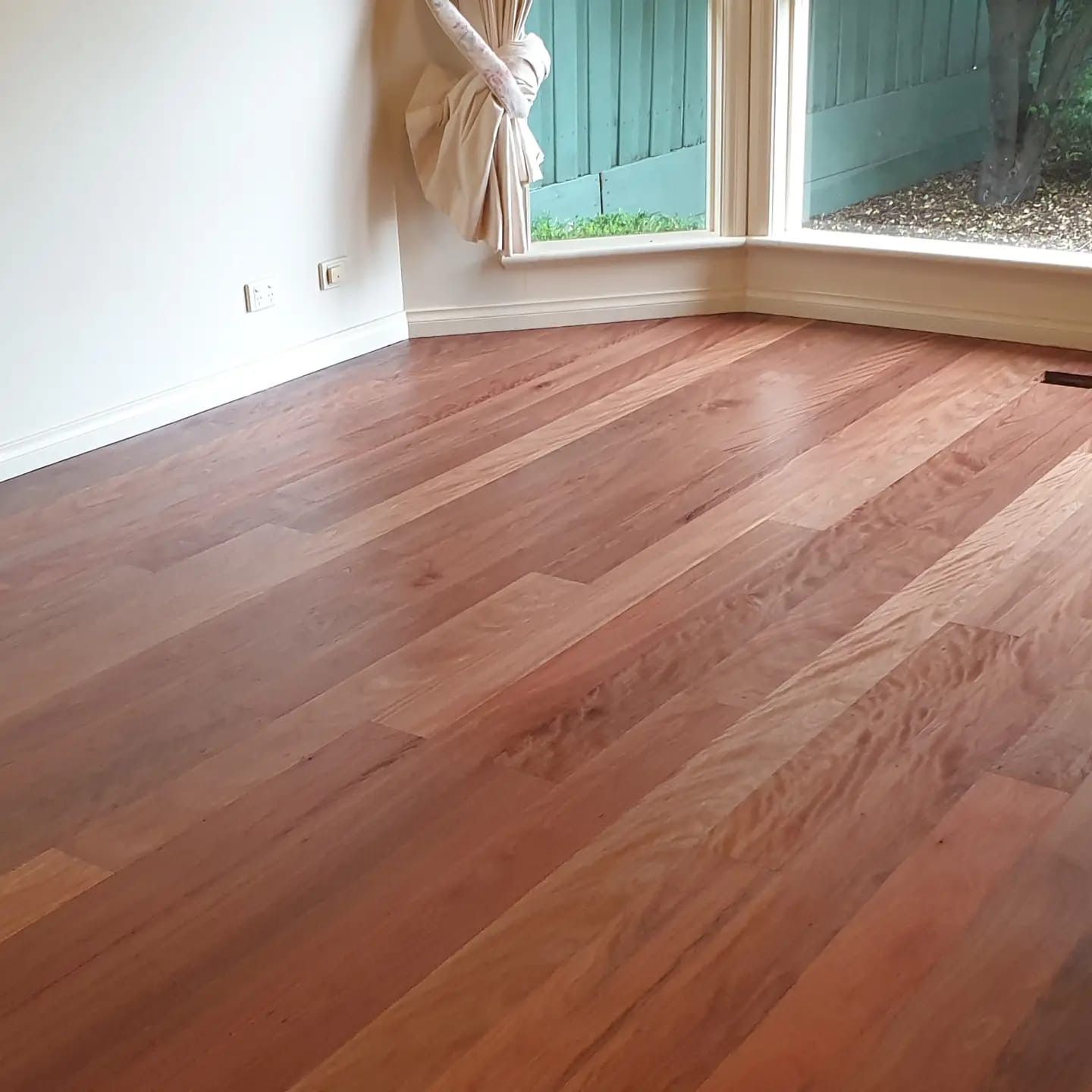 Empty room with polished wood floor, white walls, and large windows with curtains.