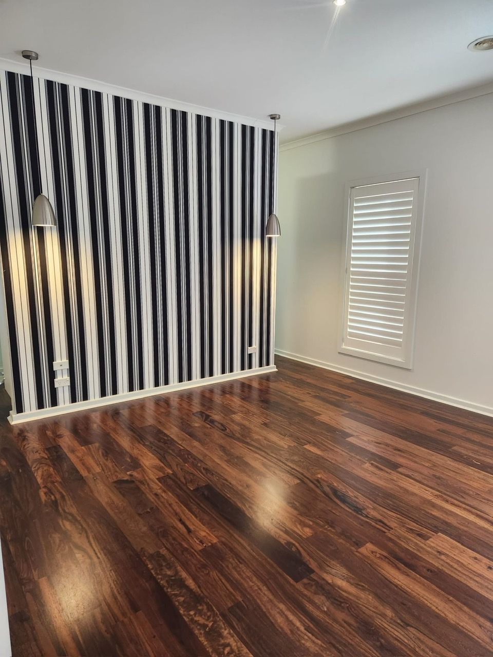 Empty room with dark wood floors, black-and-white striped accent wall, and white plantation shutters