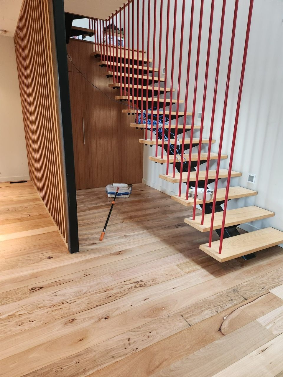 Modern indoor staircase with red cable railing and light wood steps over a wooden floor