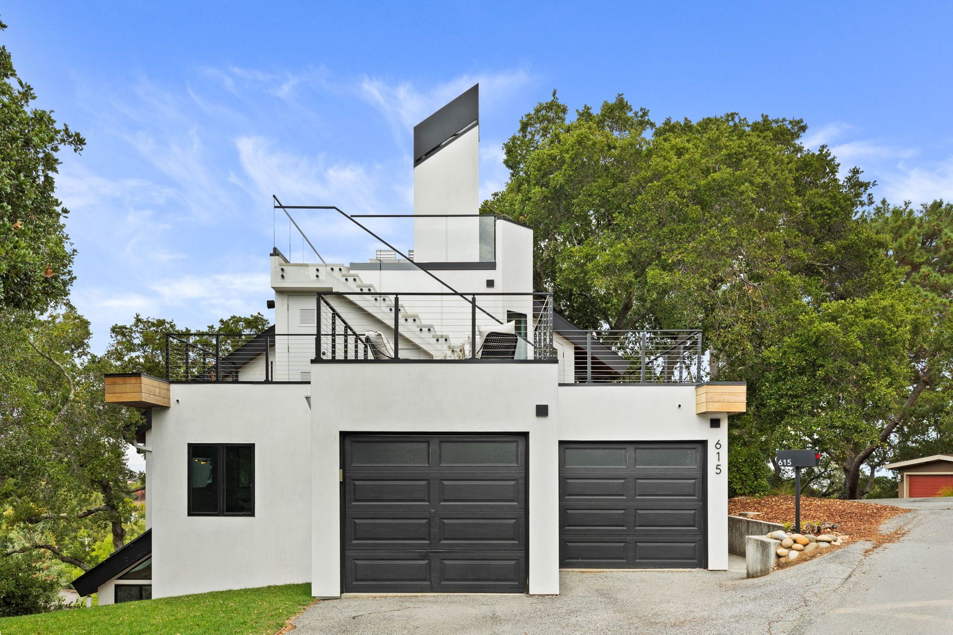 White modern house with black garage doors, deck, and angular architectural features against a blue sky.