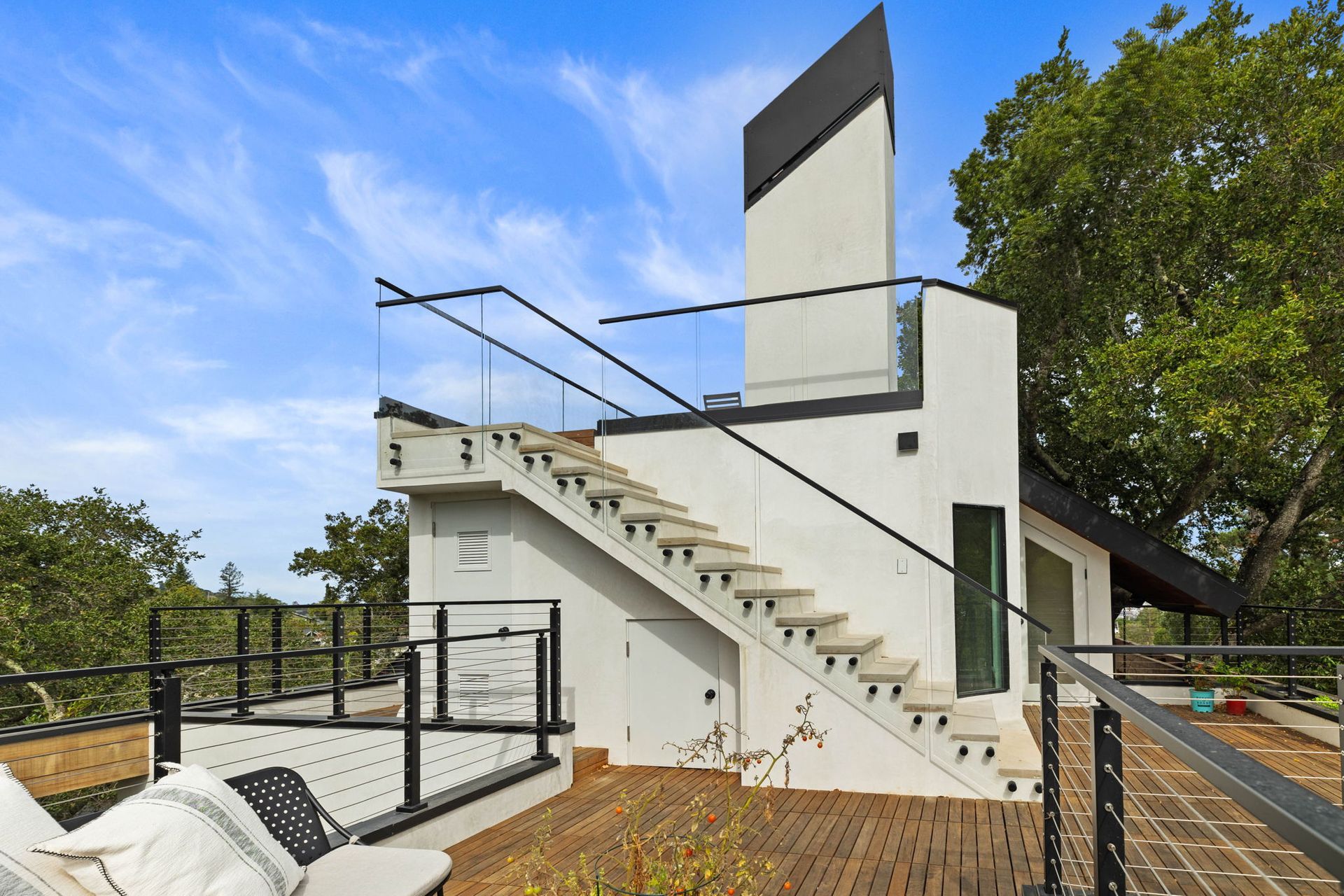 Exterior of a modern, white building with rooftop deck, stairs, glass railings, and blue sky.