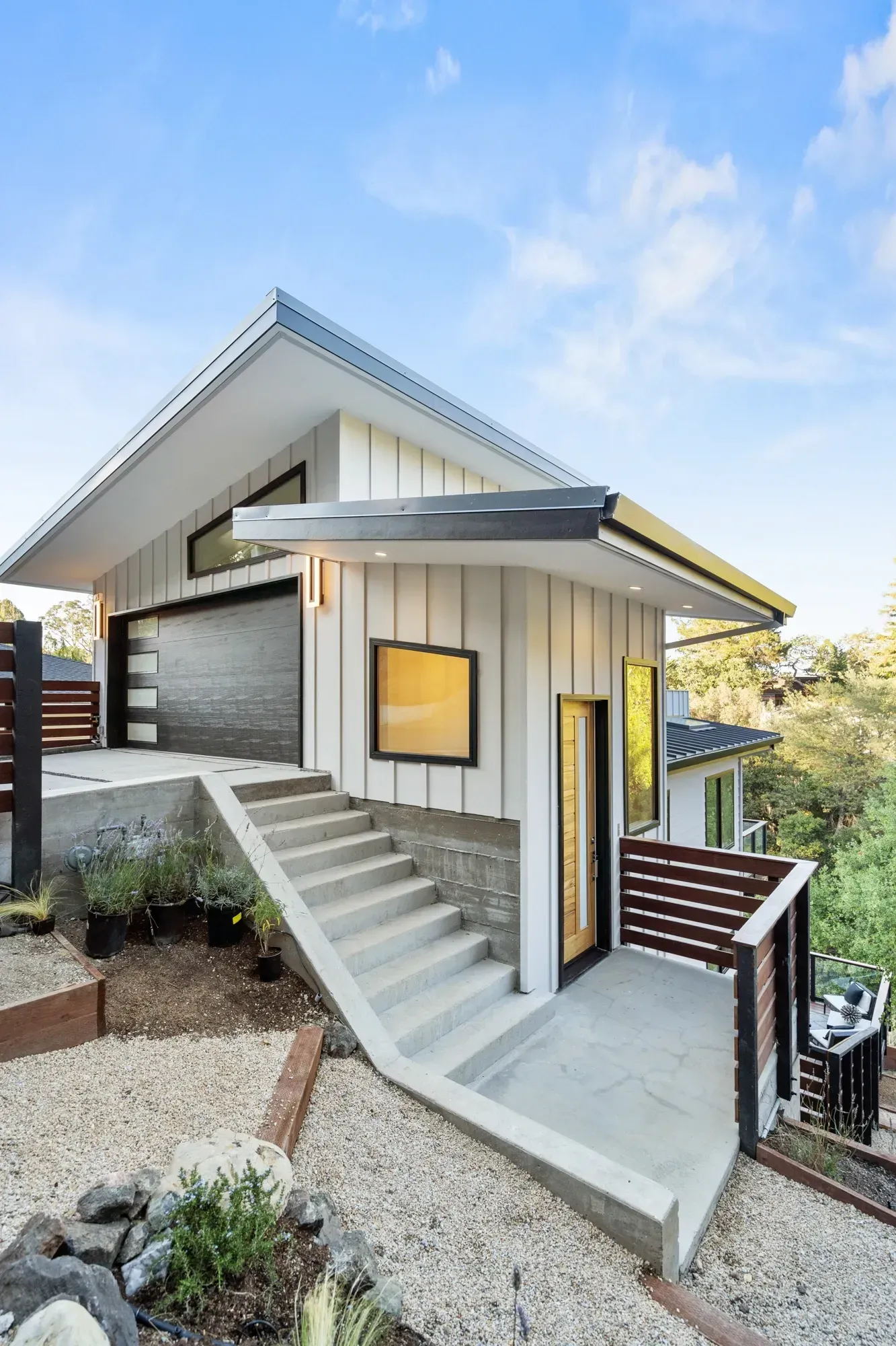 Modern white house with a sloped roof and concrete steps leading to the front door, set on a hillside.