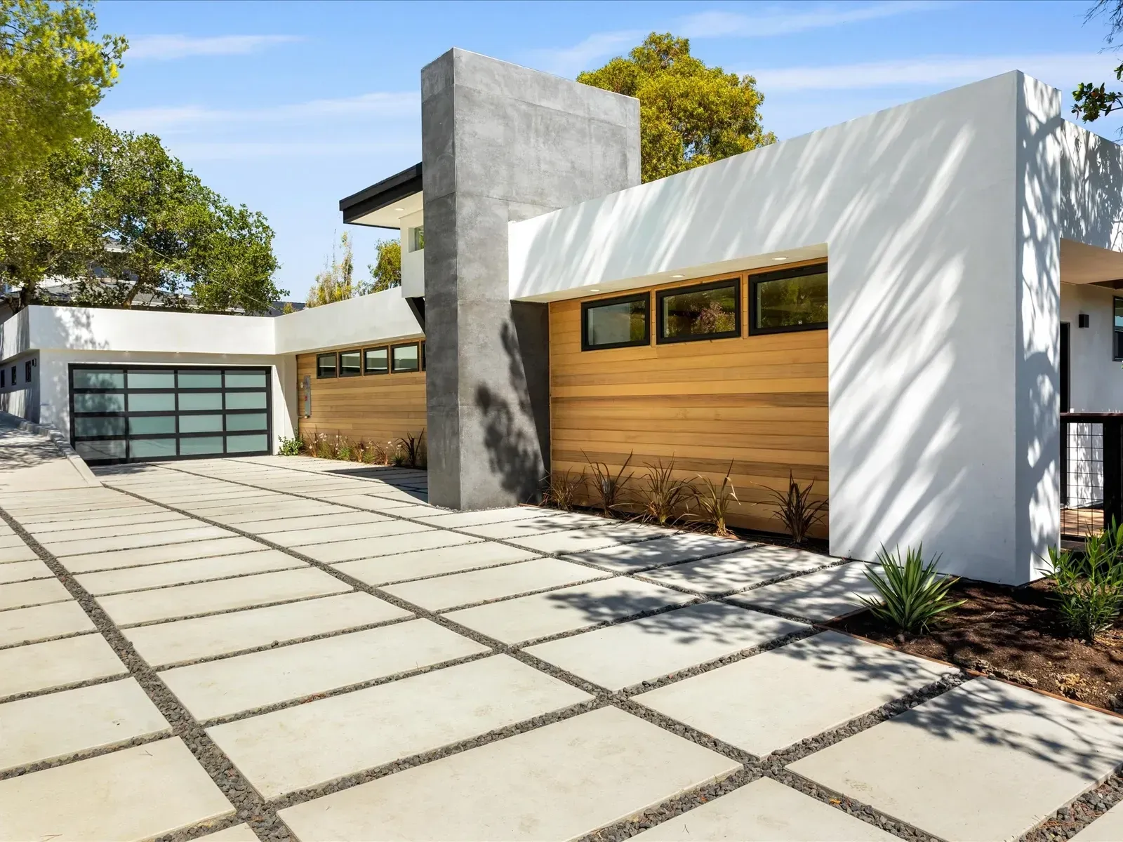 Modern white house with wood siding, gray garage door, and concrete driveway.