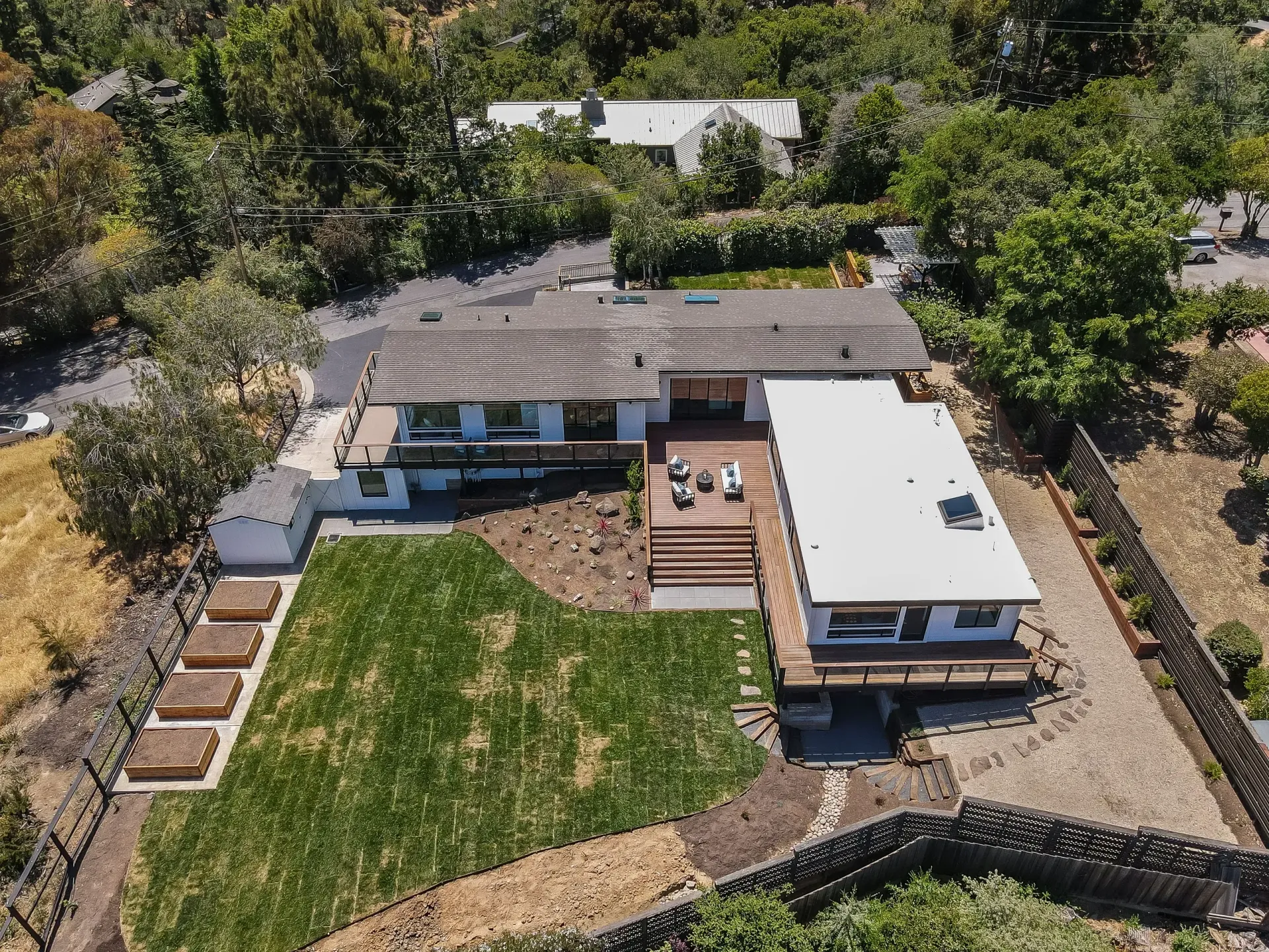 Aerial view of a house with a deck and lawn surrounded by trees and a stone wall.