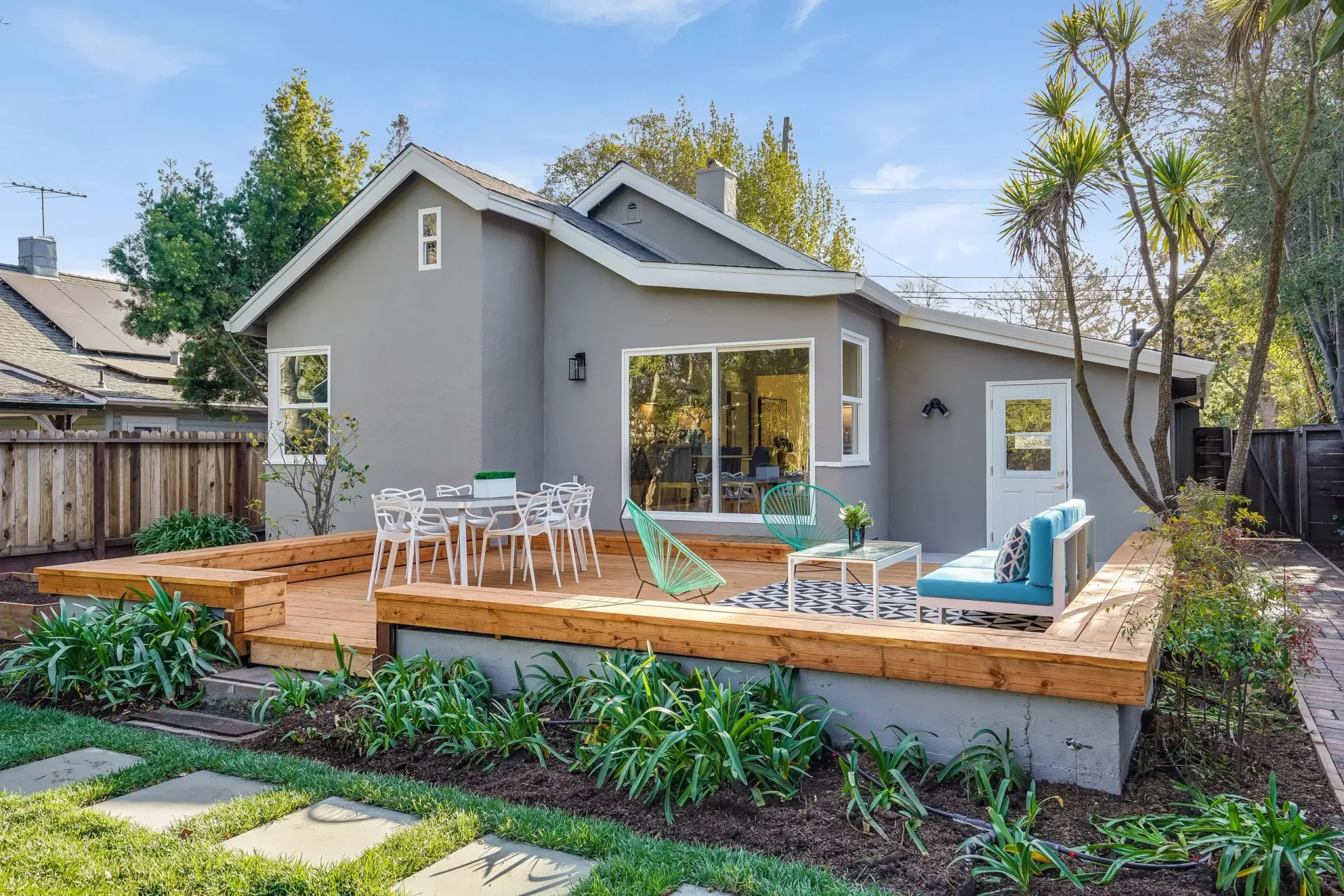 Grey house with wood deck and outdoor seating in a garden setting.