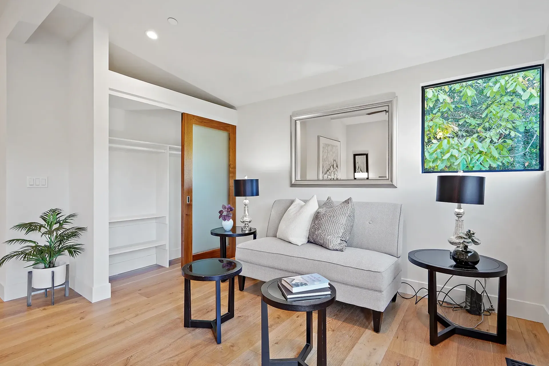 Living room with grey sofa, black tables, mirror, closet, and a mounted screen.