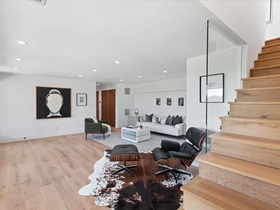 Living room with wooden floors, modern furniture, cowhide rug, and staircase.