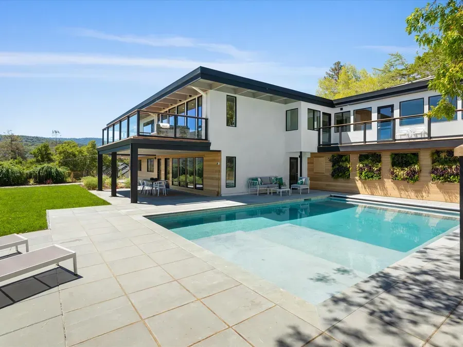Modern two-story house with a pool and outdoor seating on a sunny day.