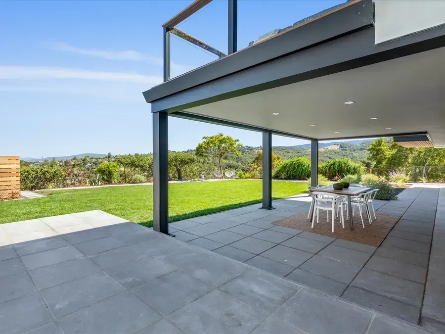 Patio with dining table, green lawn, and scenic view under a covered deck on a sunny day.