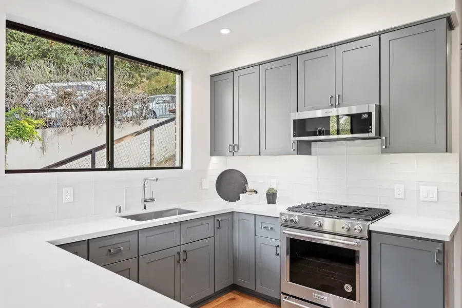 Modern gray kitchen with white countertops, stainless steel appliances, and a large window.
