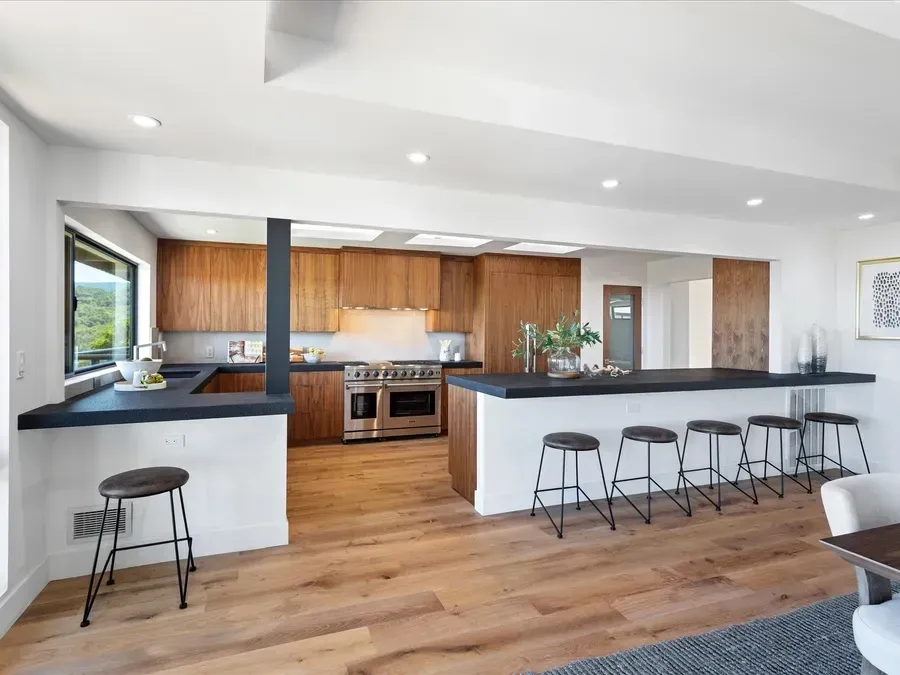 Modern kitchen with wood cabinets, black countertops, and breakfast bar with stools.