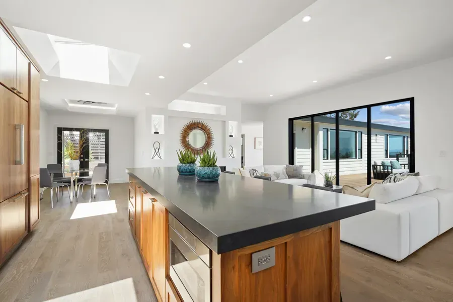 Modern kitchen with island, white walls, wood cabinets, and large sliding doors.