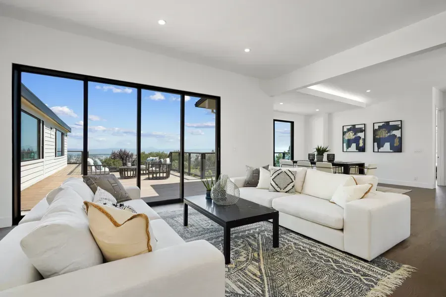 Modern living room with white sofas, black coffee table, sliding glass door with a view.