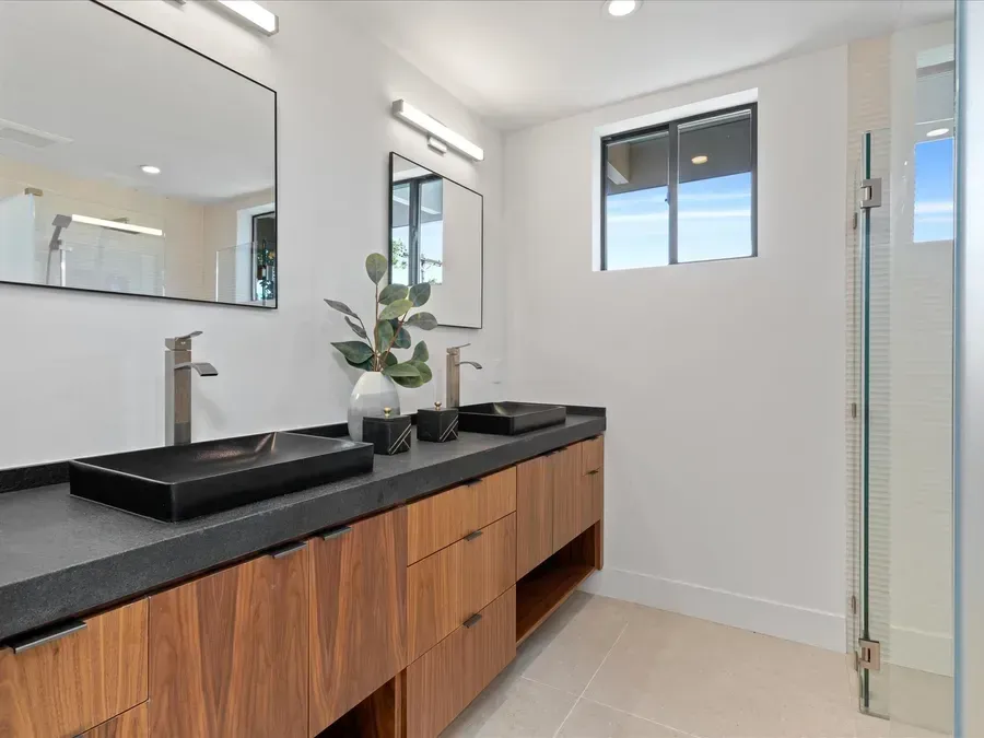Modern bathroom with wooden vanity, black sinks, and large mirrors.