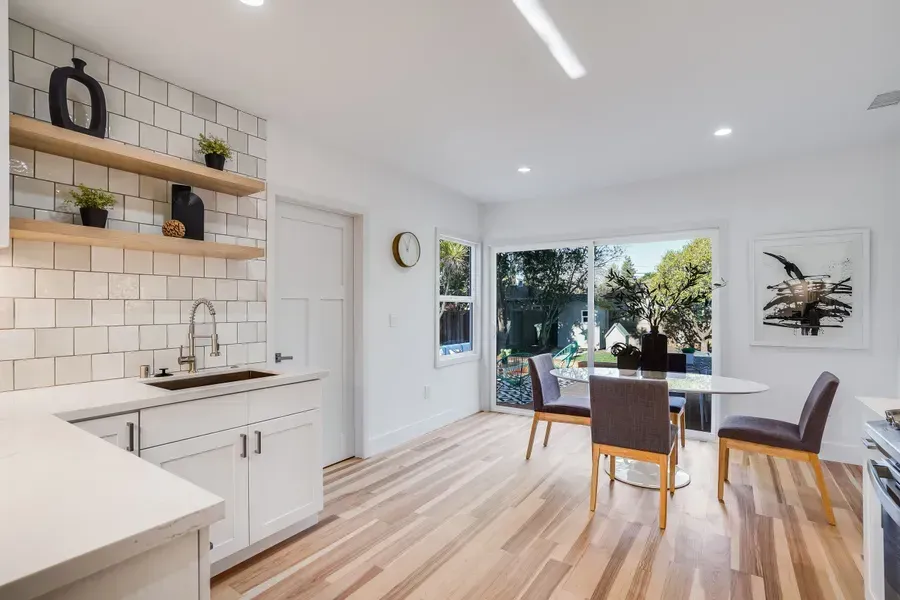 Bright kitchen with white cabinets, wood floors, and a dining table by sliding doors.