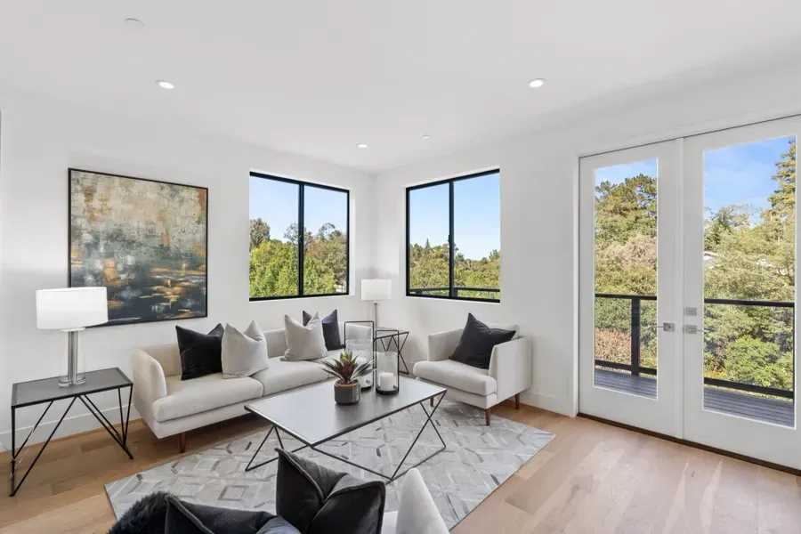 Modern living room with white walls, light wood floors, and floor-to-ceiling windows with a balcony view.