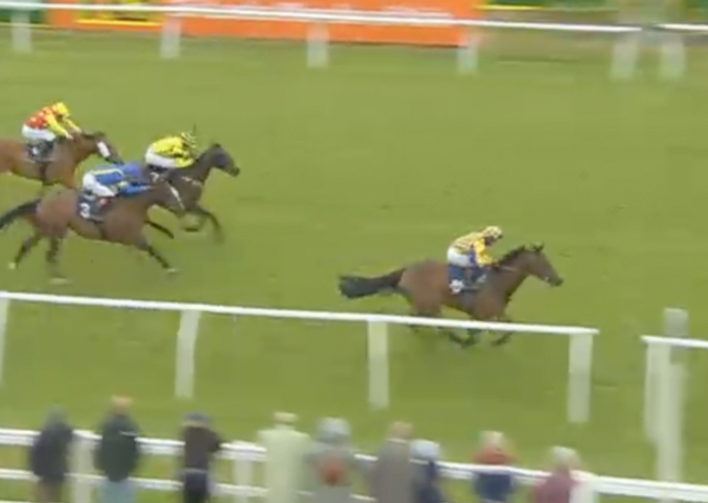 Horse race with three jockeys racing on a grassy track, one horse leading near the rail