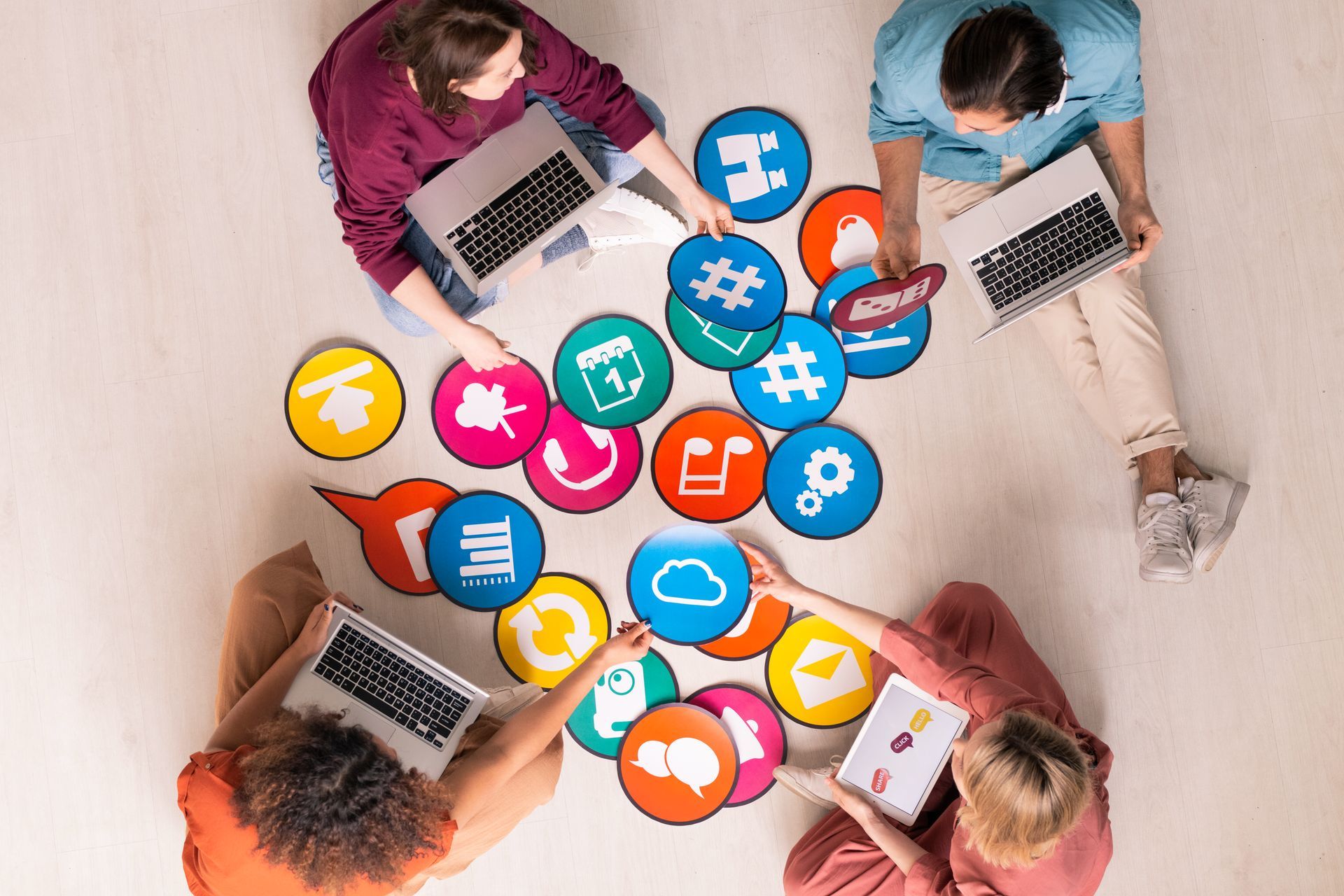 A group of people are sitting on the floor with laptops and social media icons.