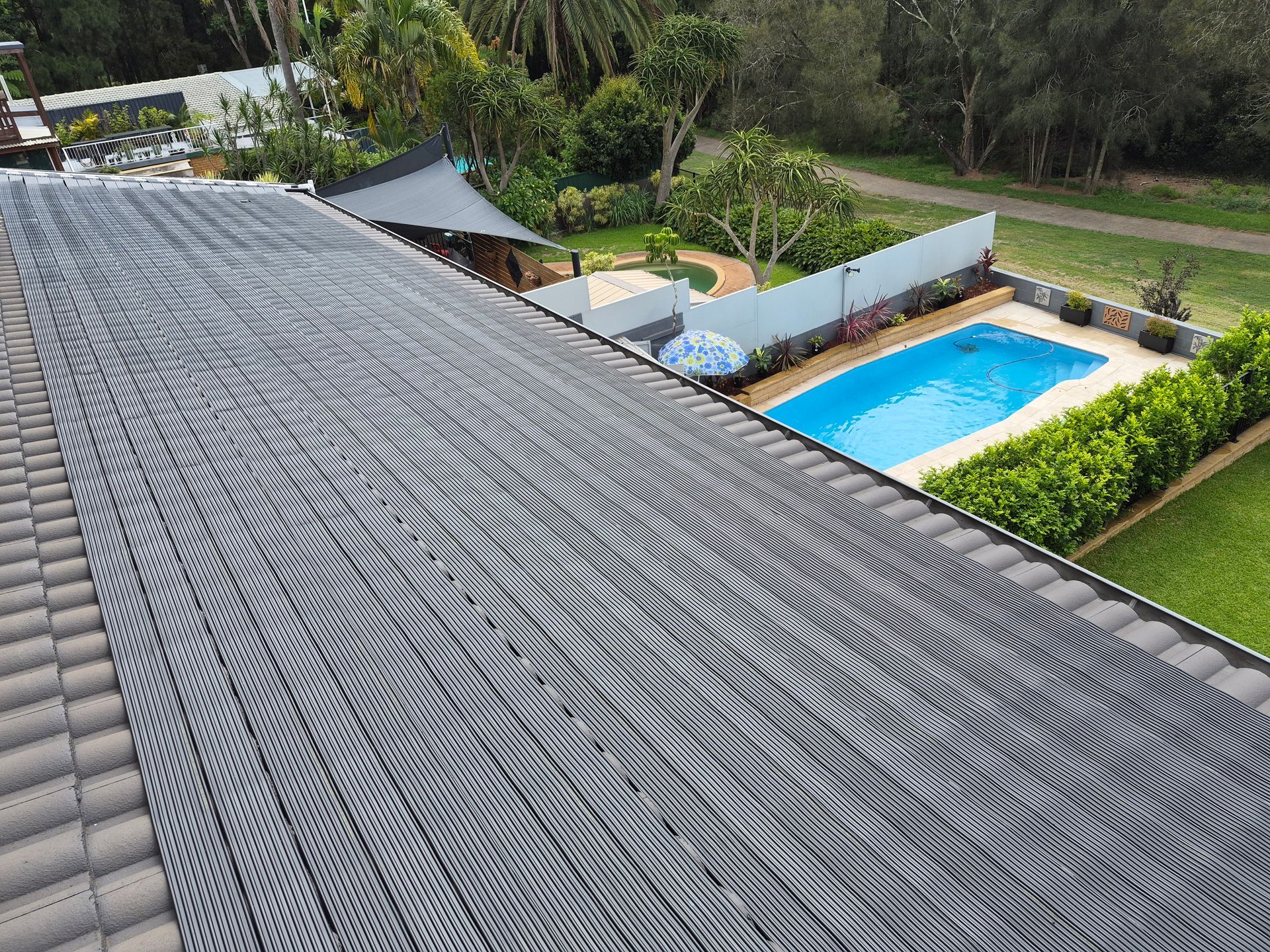 Rooftop solar panels on a tiled roof overlooking a backyard with a pool and lush greenery — Solar Services in Erina, NSW