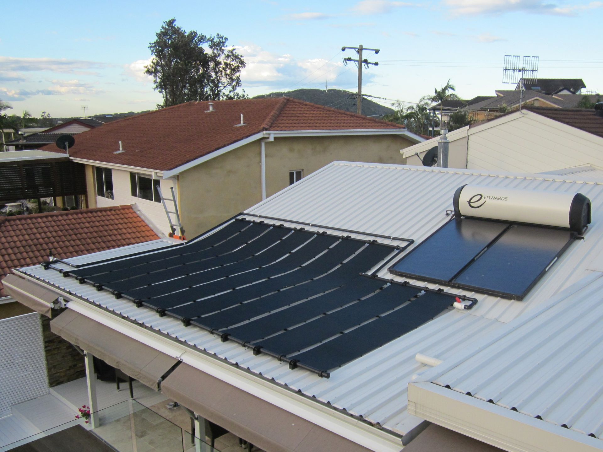 Solar Panels Installed on A Dark Tiled Roof Against a Blue Sky — Solar Services in Erina, NSW