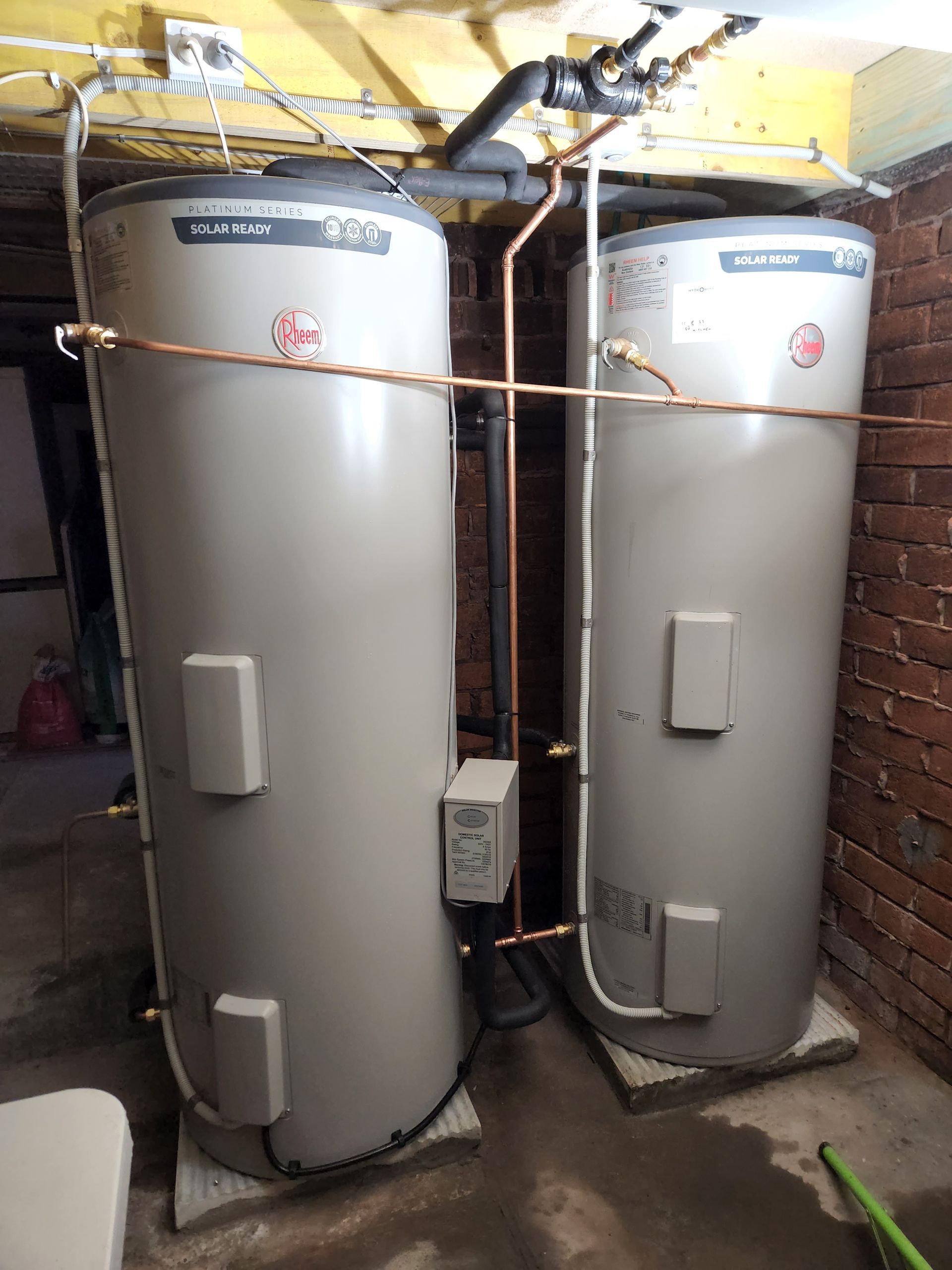 two hot water heaters next to each other in front of a brick wall — Solar Services in Erina, NSW