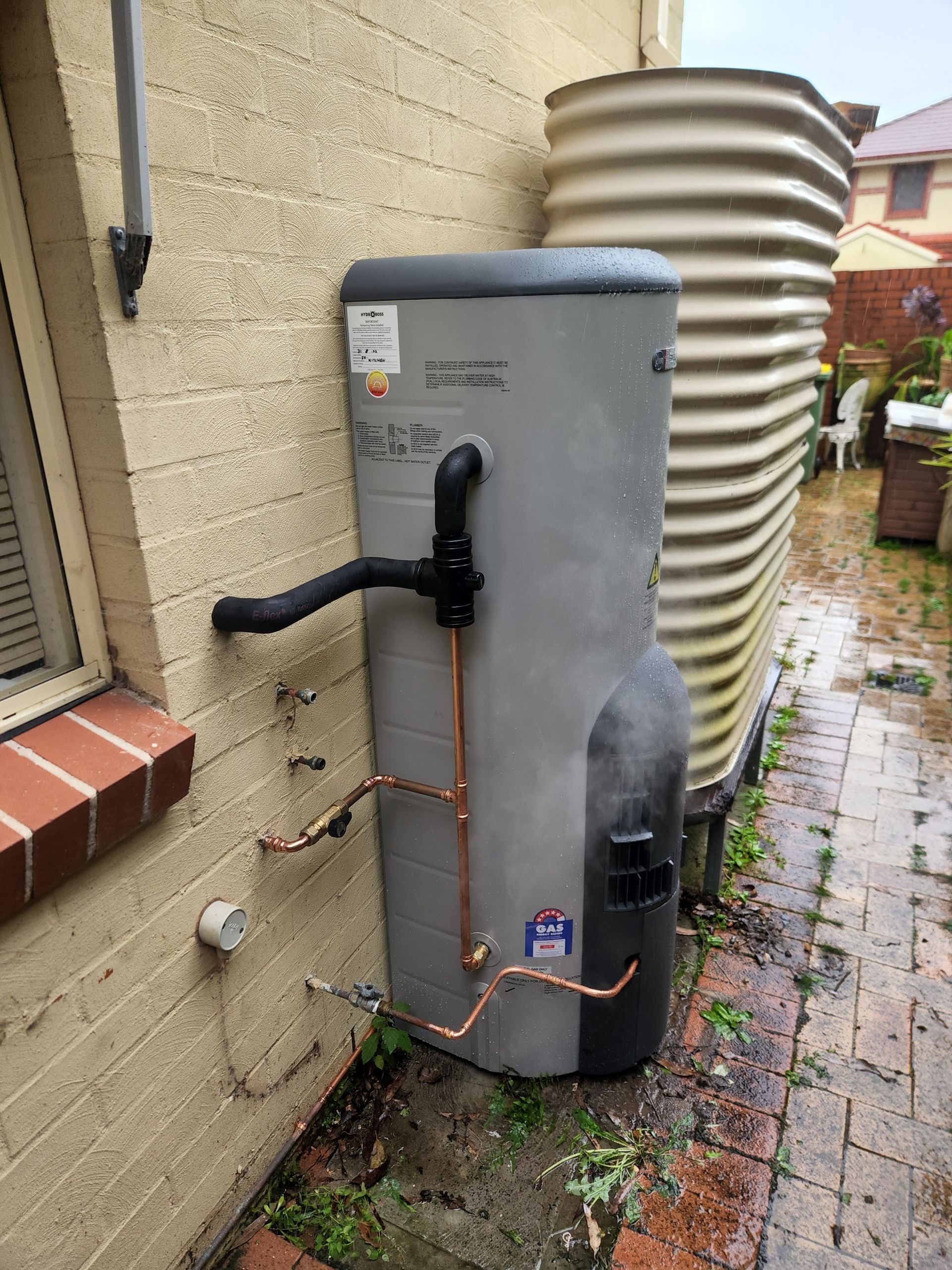 A Water Heater is Attached to the Side of a Brick Building — Solar Services in Erina, NSW