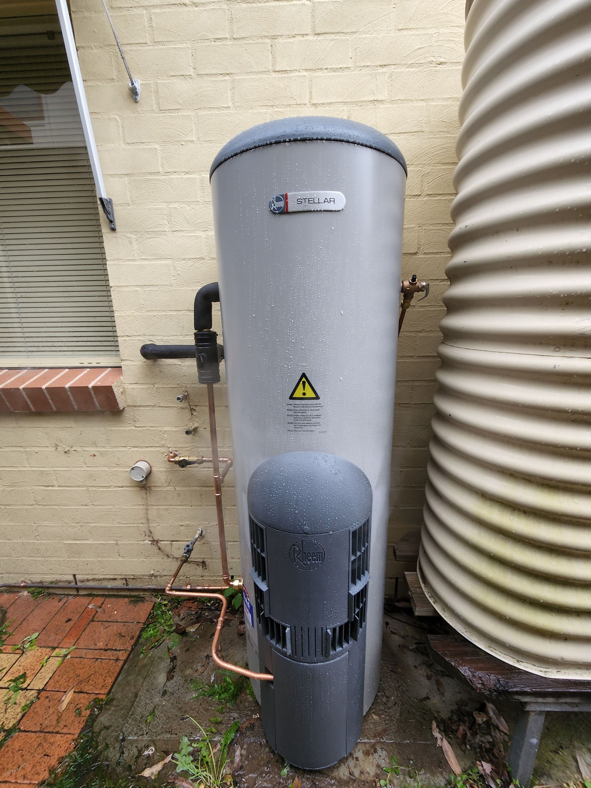 A Water Heater is Attached to the Side of a Brick Building — Solar Services in Erina, NSW