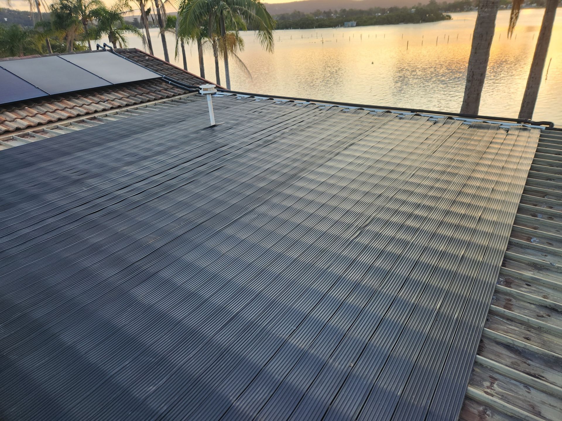 Rooftop covered with Gulfstream Solar Pool Heating beside a calm waterfront at sunset.