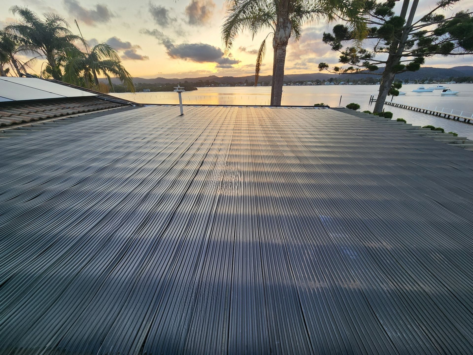 Wooden deck overlooking water at sunset, with palm trees and a cloudy sky — Solar Services in Erina, NSW