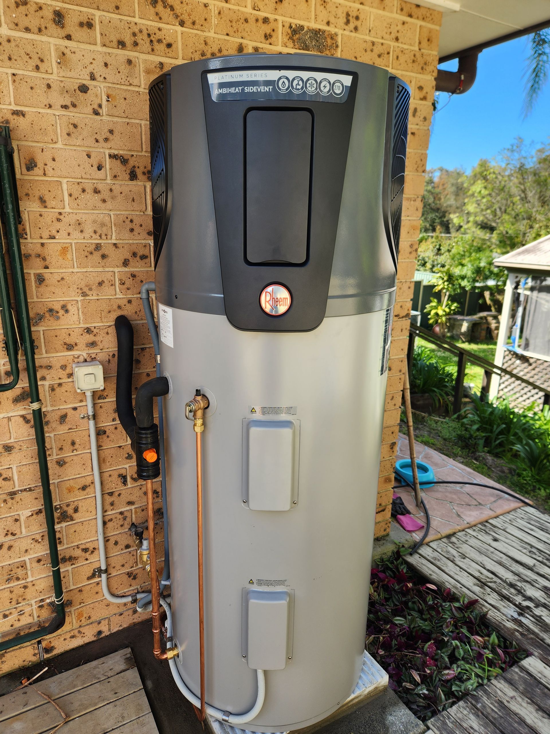 a grey large cylinder for water heating next to a brick wall — Solar Services in Erina, NSW