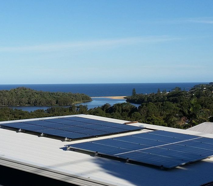 Solar panels on a rooftop overlooking a blue ocean and lush islands under a clear sky — Solar Services in Erina, NSW